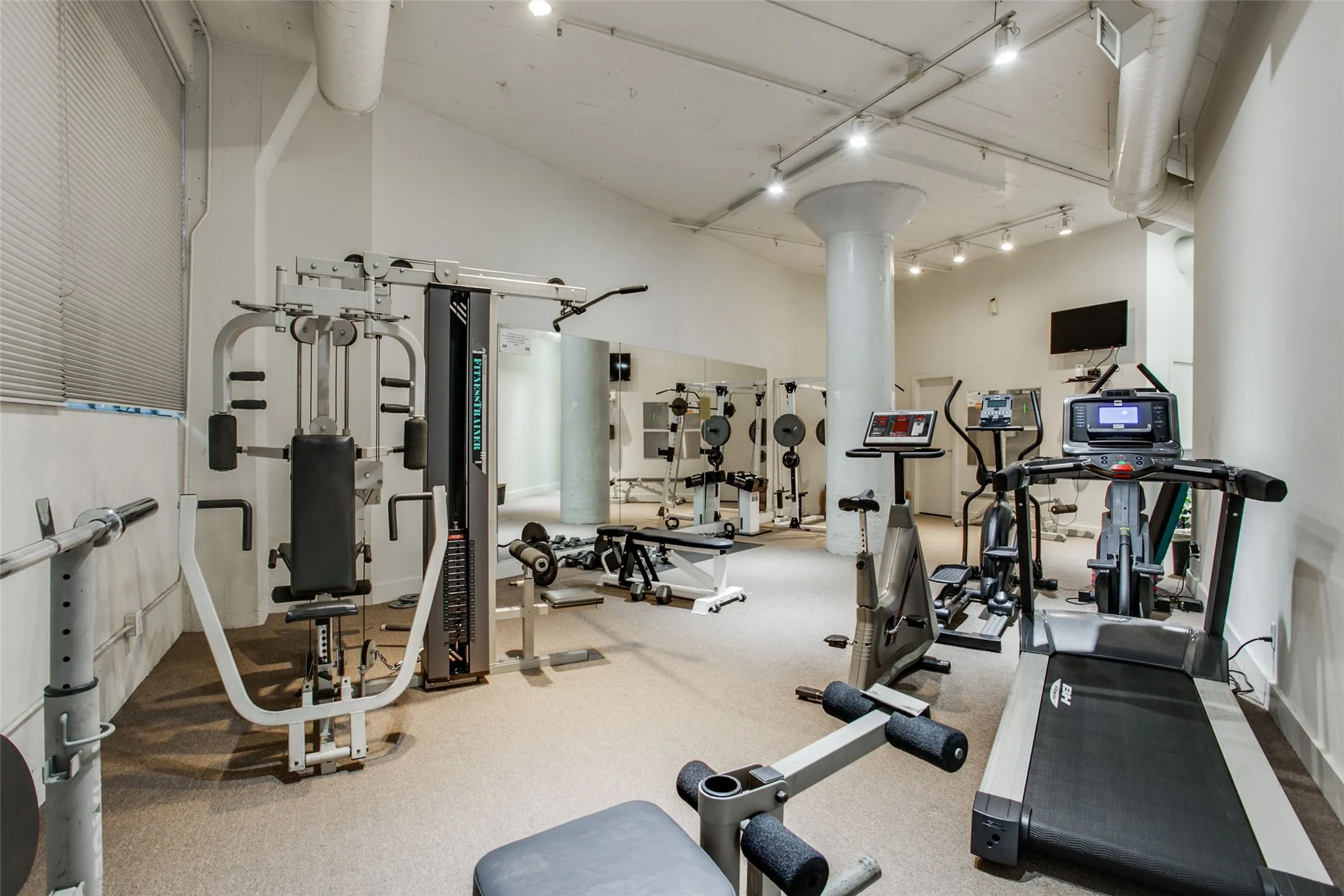 Fitness center featuring carpet flooring, exposed ductwork, track lighting, and a wall-mounted television