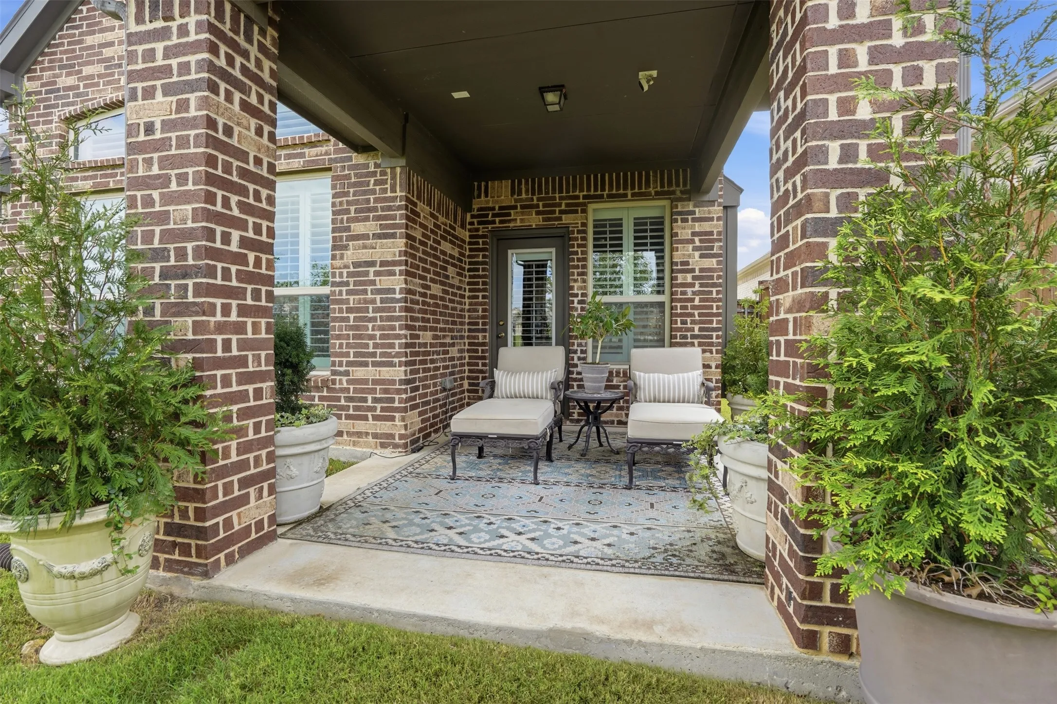 Covered patio featuring brick columns, a concrete floor, and an outdoor rug