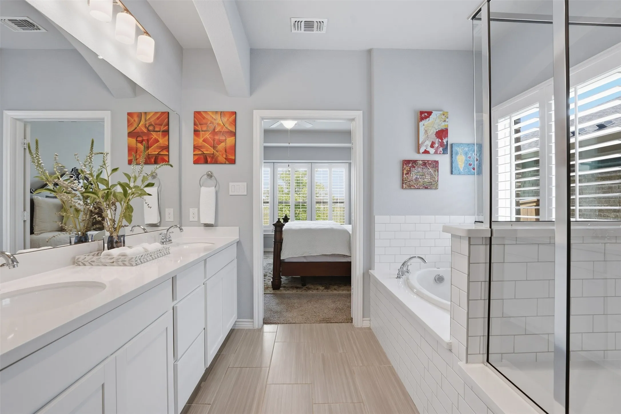 Bathroom featuring dual vanity with undermount sinks, a built-in tub with subway tile surround, a glass-enclosed shower, and wood-finish flooring