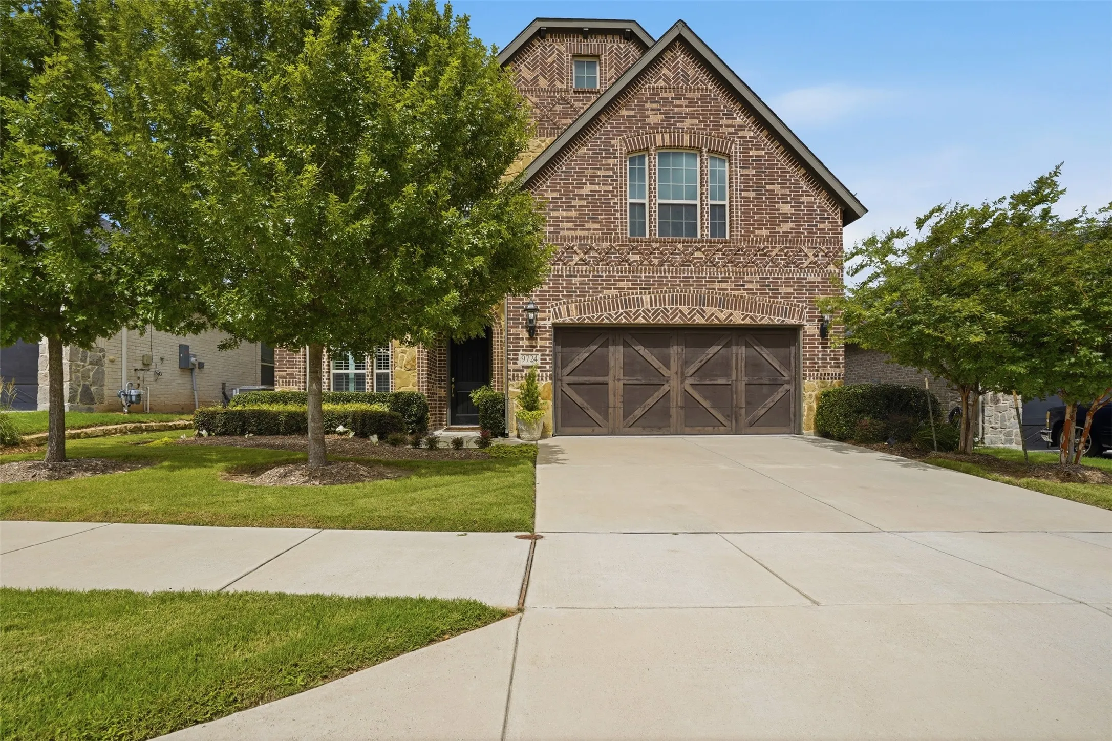 Brick facade home with a prominent gabled roofline and an integrated two-car garage featuring decorative wood-finish doors