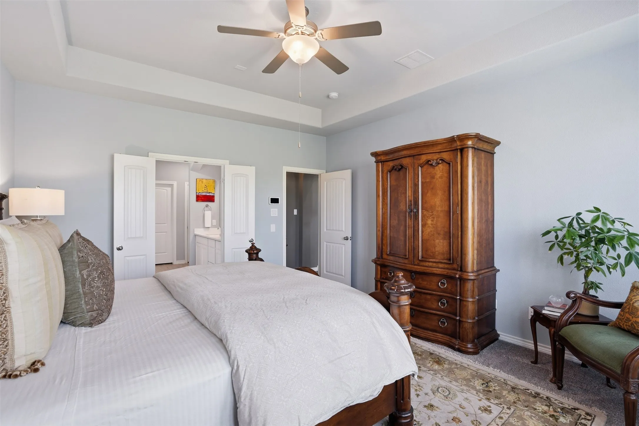 Bedroom featuring a tray ceiling with a ceiling fan, light blue painted walls, and gray carpeting