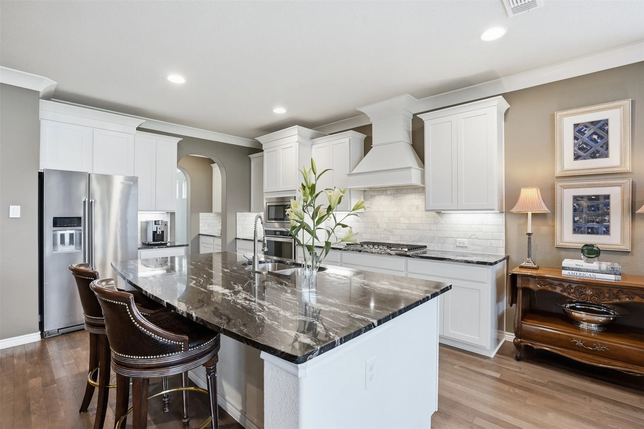 Spacious kitchen featuring an oversized island with a dark granite countertop, white shaker cabinetry, stainless steel appliances, and wood-finish flooring