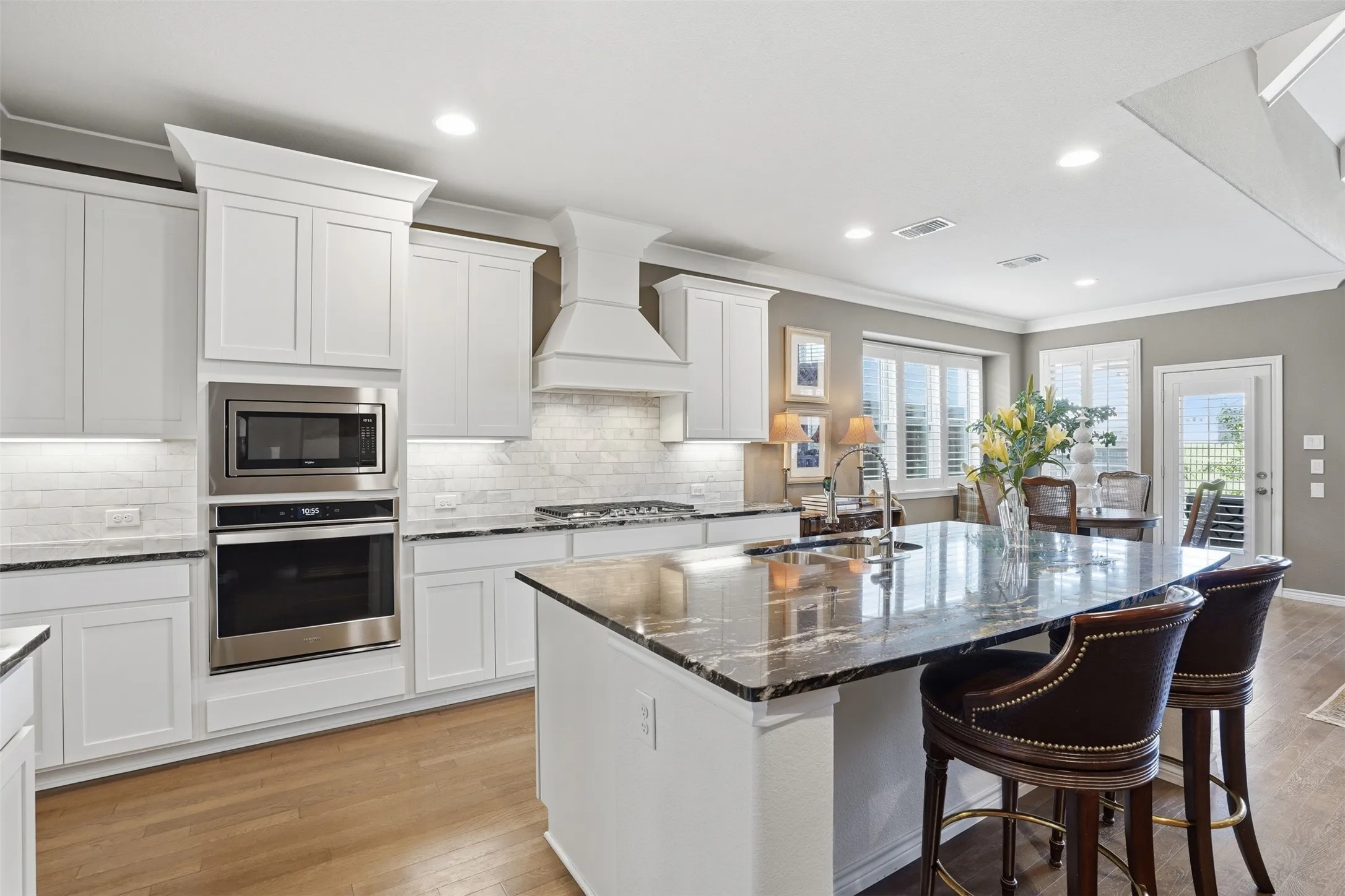 Spacious kitchen featuring an expansive island with a polished countertop, white shaker-style cabinetry, stainless steel appliances, a tile backsplash, and wood-finish flooring