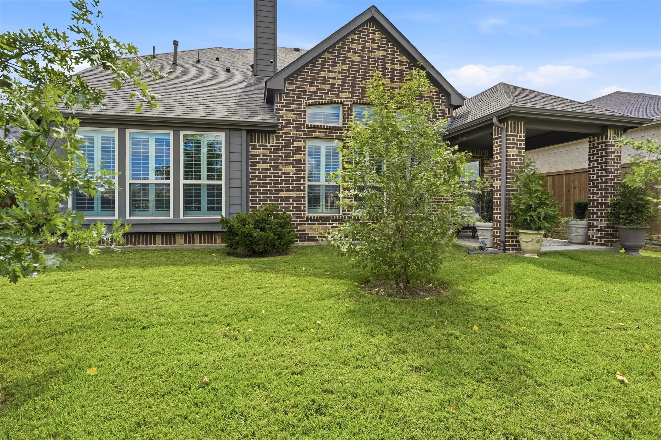 Spacious backyard featuring a covered patio, brick columns, and a mature tree