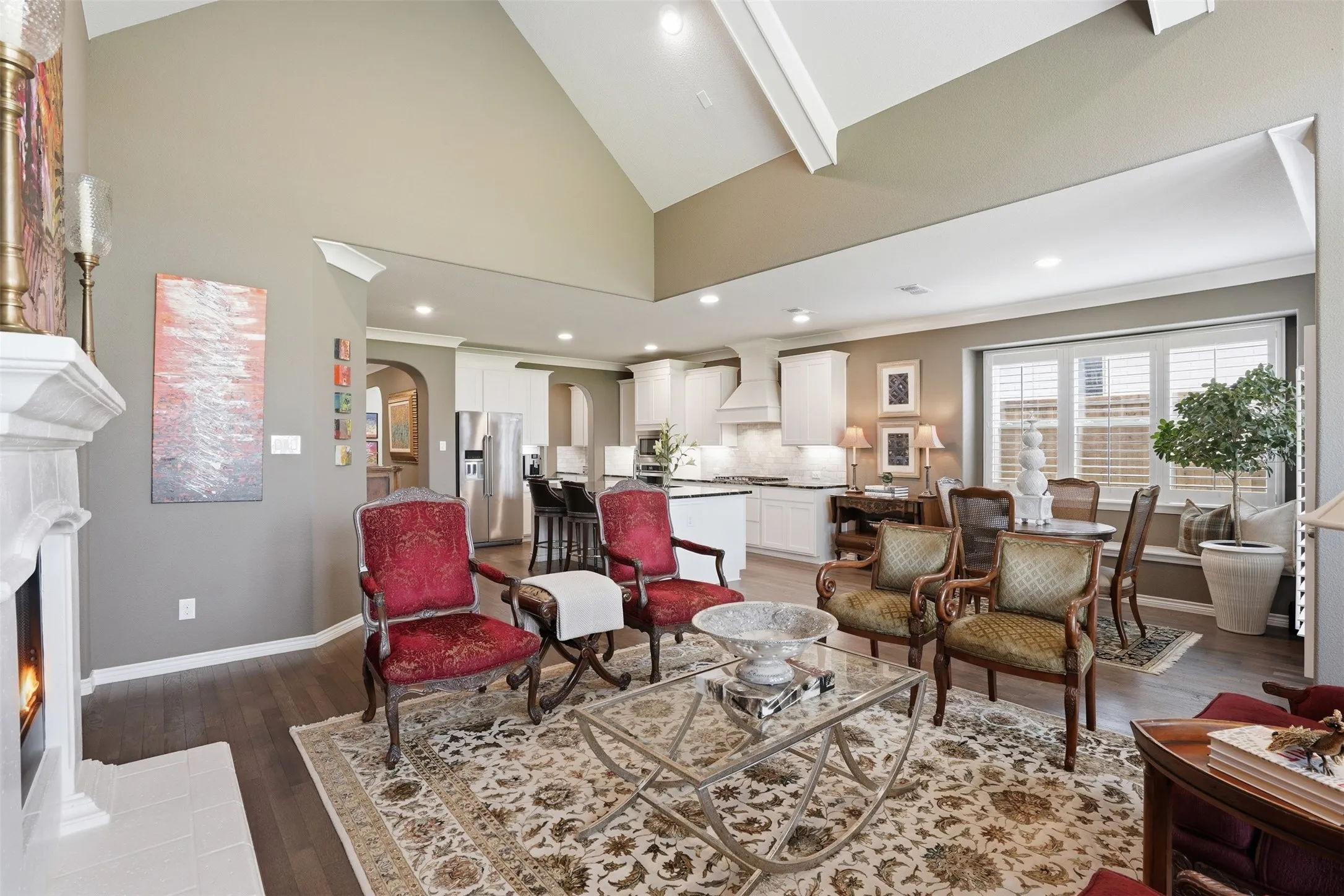 Spacious living area featuring a vaulted ceiling with exposed beams, an ornate fireplace with a white mantel, and wood-finish flooring