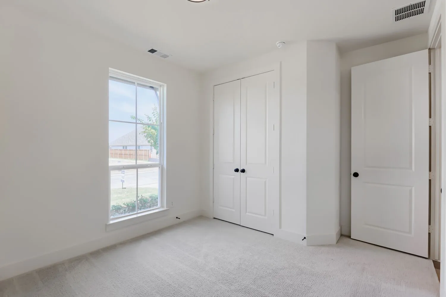 Bright secondary bedroom featuring neutral carpet flooring, dual closets with black hardware, and large windows providing natural light