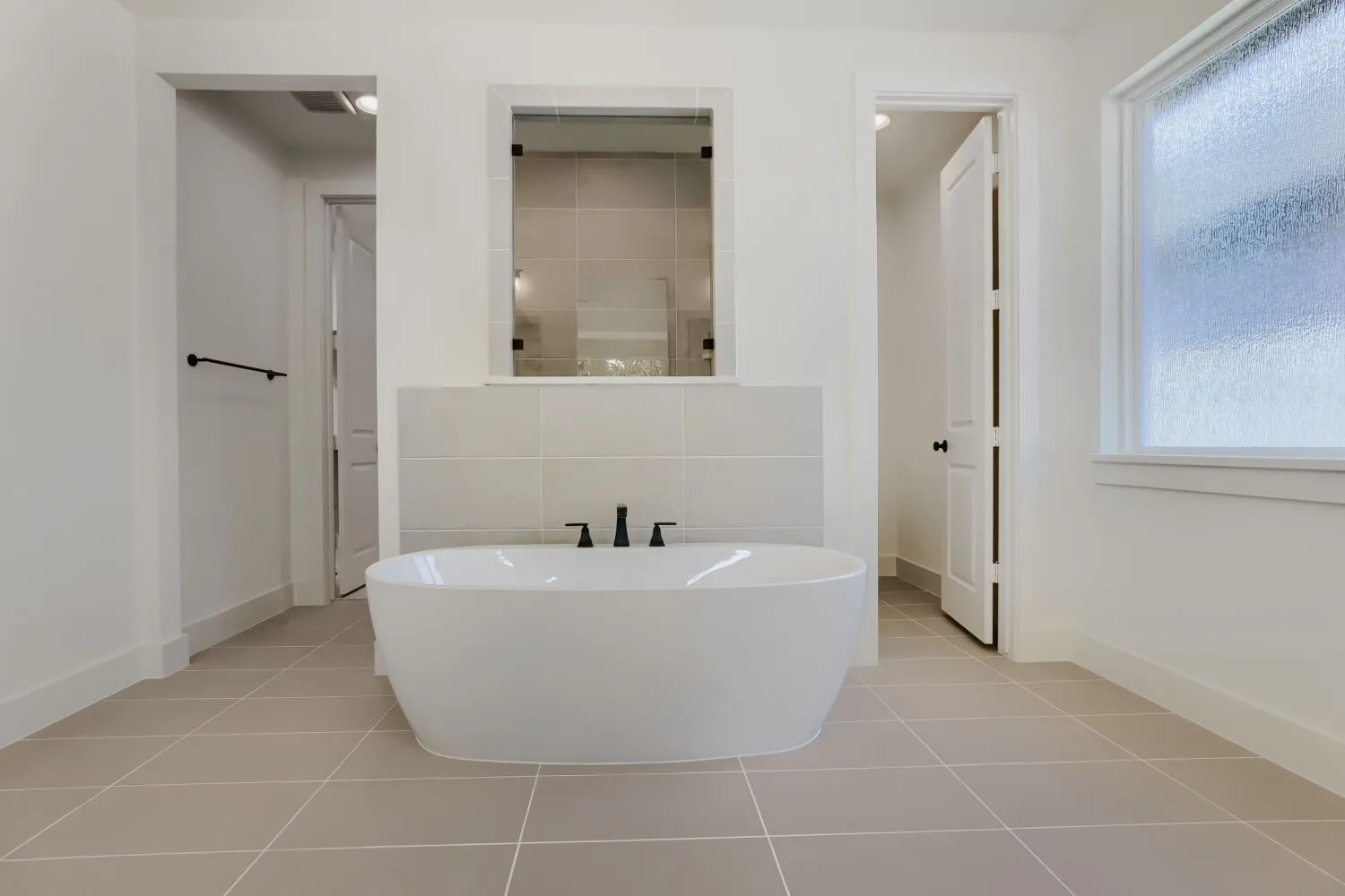 Freestanding soaking tub with matte black fixtures, set on large format floor tiling