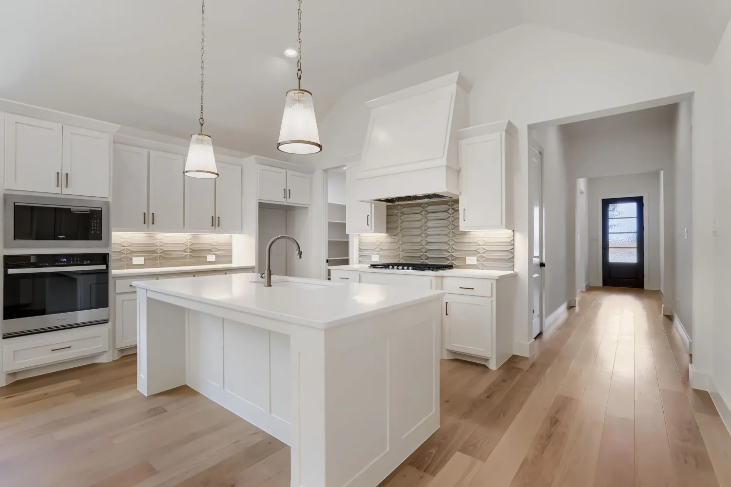 Expansive kitchen with a vaulted ceiling, white cabinetry, integrated stainless steel appliances, a center island with sink, and light wood-finish flooring