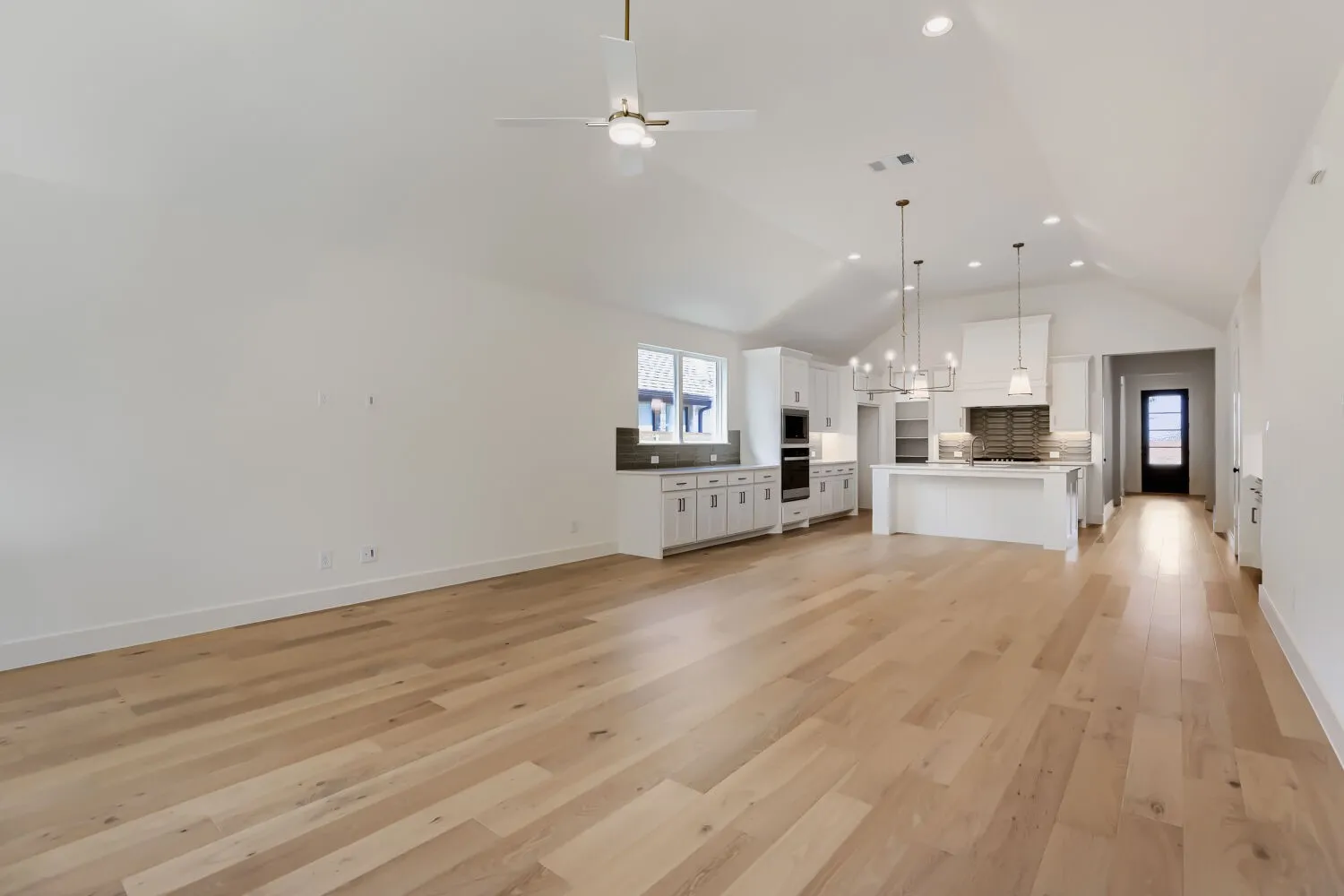 Vaulted ceiling, recessed lighting, wood-finish flooring, white shaker cabinetry, and a large kitchen island with pendant lighting