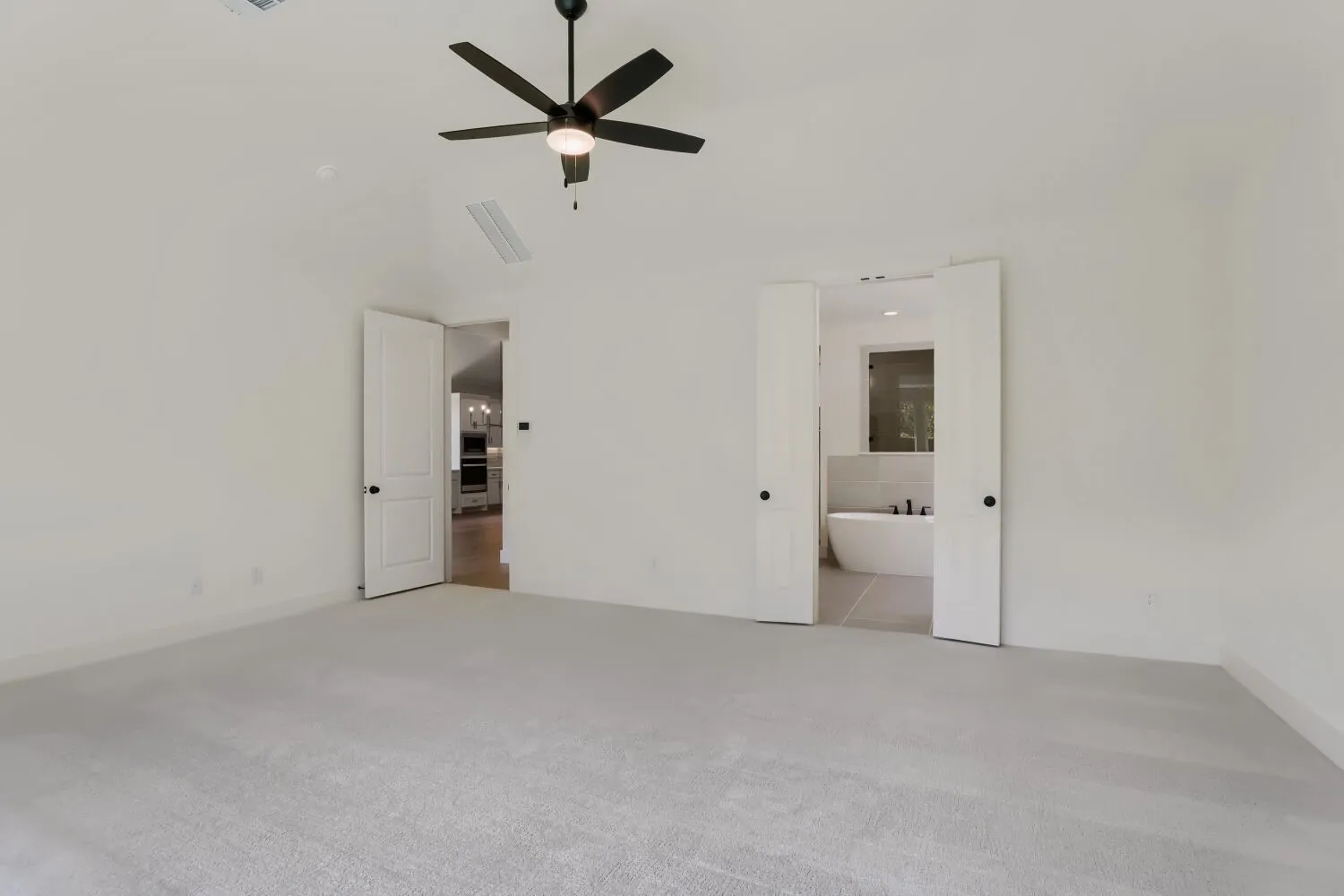 Vaulted ceiling with a black ceiling fan, light-toned carpet, and white interior doors