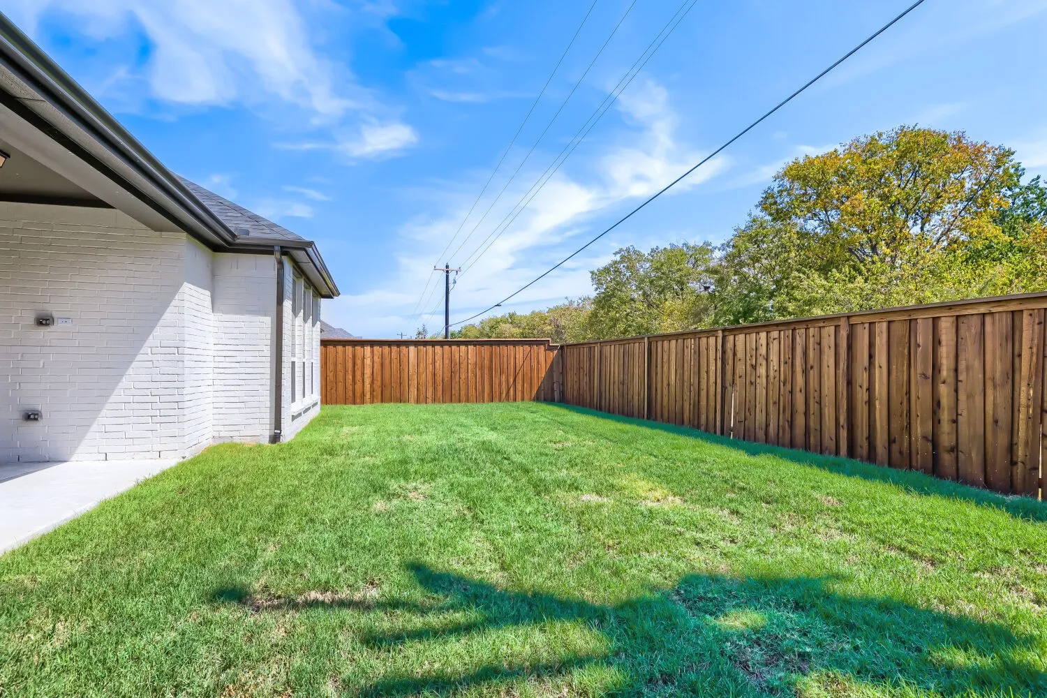 Expansive green lawn, wood privacy fence, white brick exterior, covered patio, and dark shingle roof