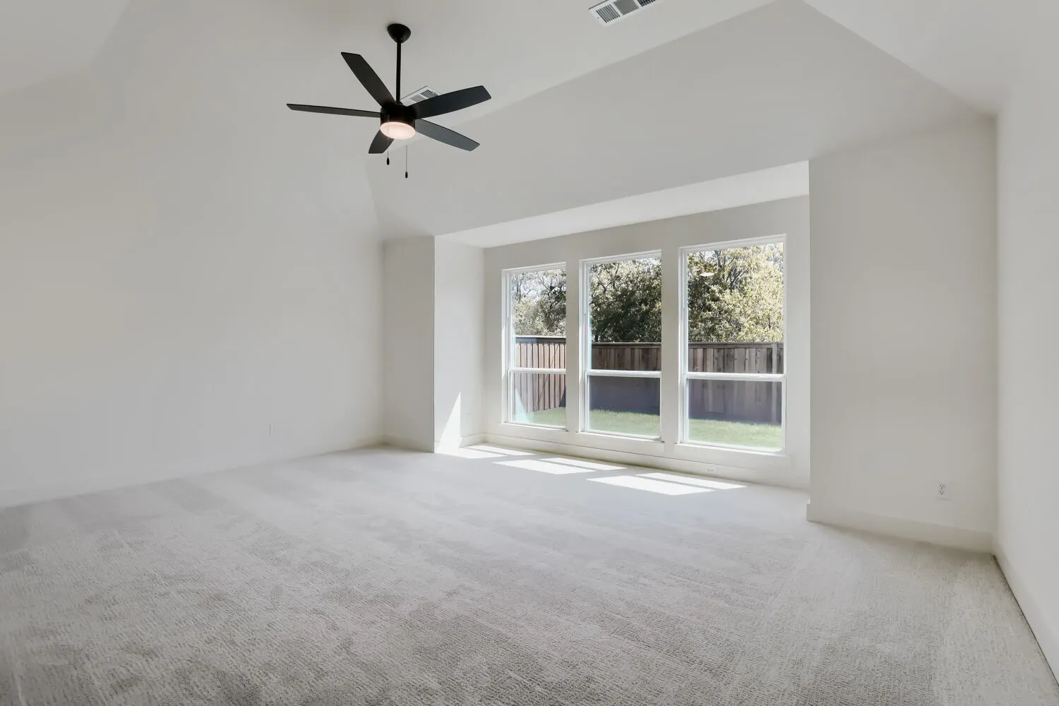 Recessed ceiling, three large windows, light gray carpet, black ceiling fan, and white walls