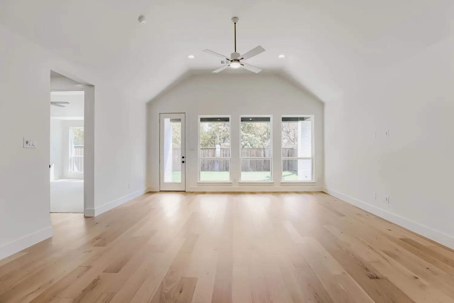 Spacious primary living area showcasing soaring vaulted ceilings, hardwood flooring throughout, and abundant natural light from a wall of French doors opening to the rear grounds