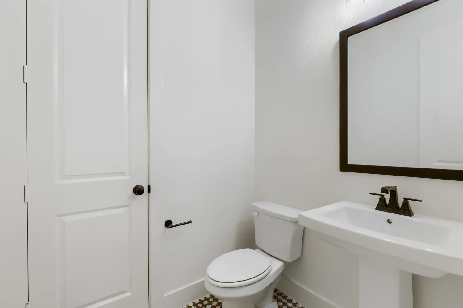 Pedestal sink with dark bronze fixtures and a framed mirror