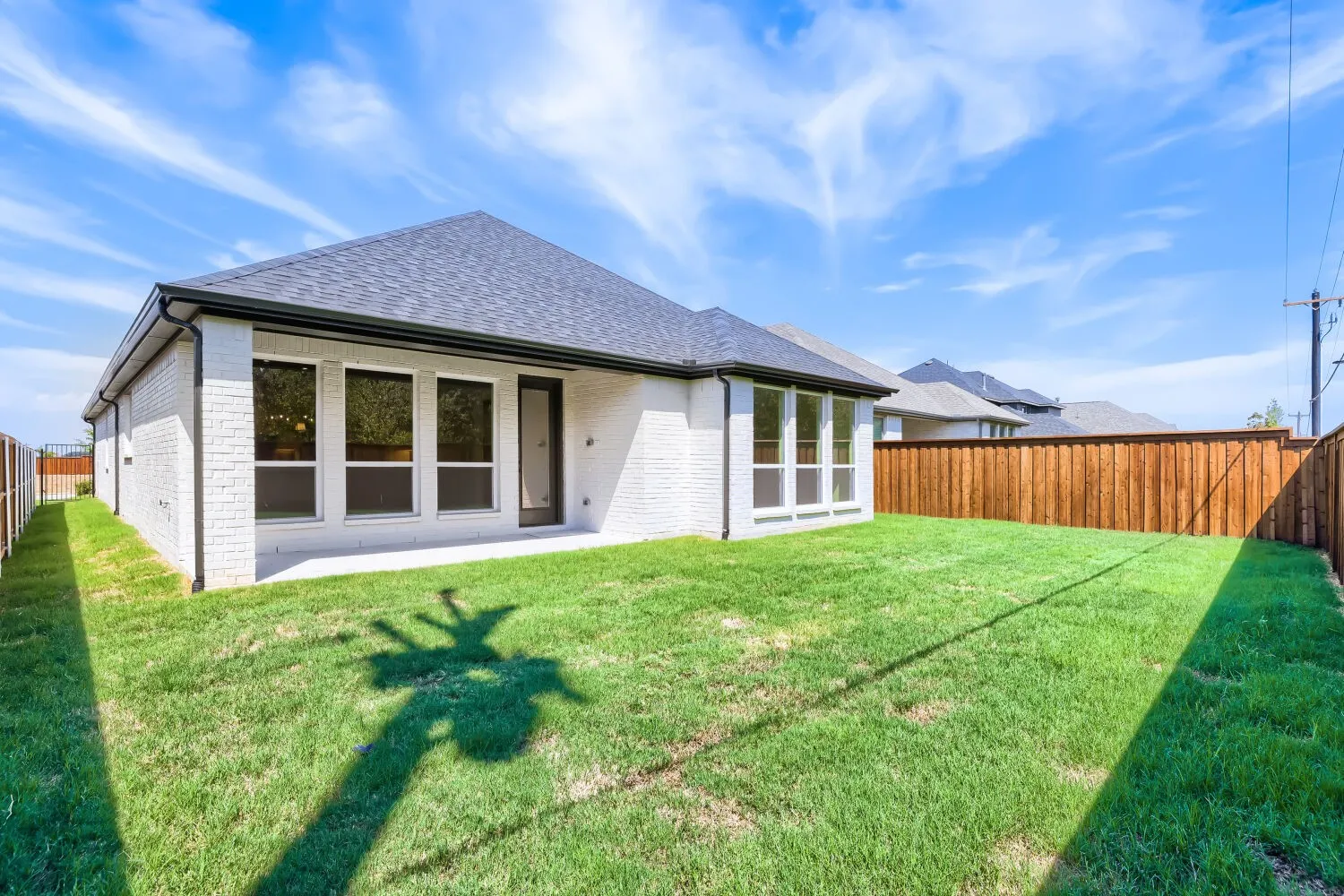 Expansive backyard featuring a manicured lawn, wood fencing, and a concrete patio