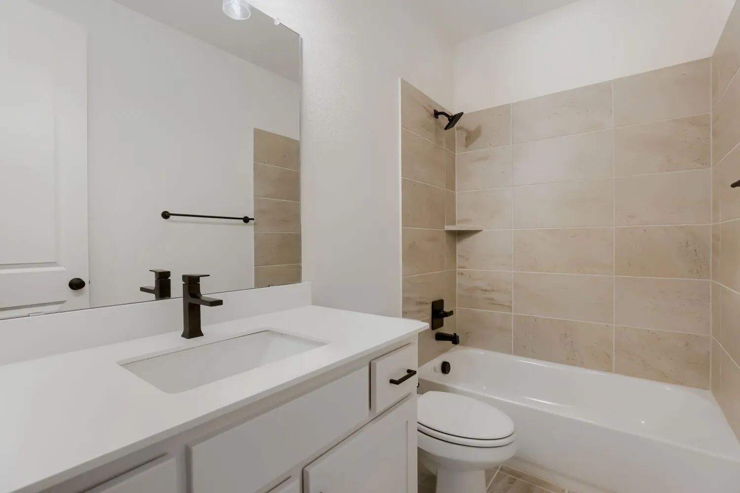 Bathroom featuring a white vanity with integrated sink, dark bronze fixtures, subway tile shower surround, and a built-in shower shelf