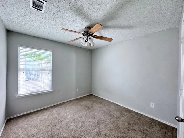 Carpeted room featuring a ceiling fan with light fixture, window with blinds, and neutral grey wall paint