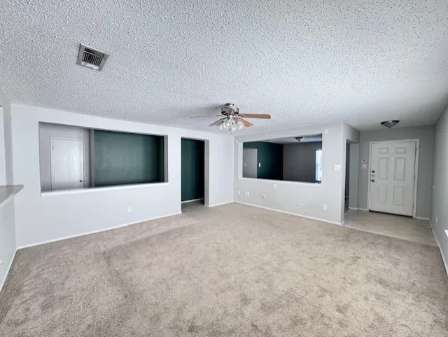 Spacious living area featuring neutral carpeting, a ceiling fan with integrated lighting, and a white paneled entry door