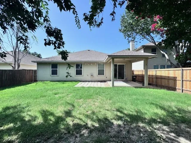 Expansive backyard featuring a covered patio, a sliding glass door, and a manicured lawn