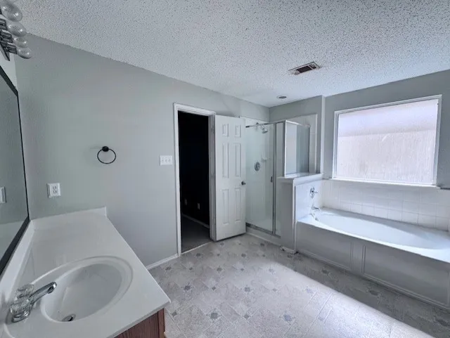 Spacious bathroom featuring a single vanity with an integrated sink, a separate shower enclosure with a glass door, and an oversized soaking tub