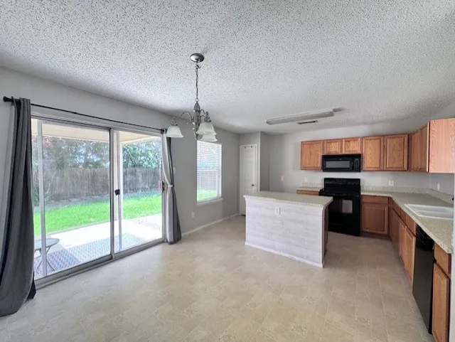 Kitchen and dining area featuring a central island, wood cabinetry, black appliances, and tile flooring