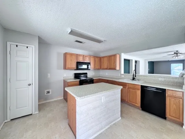 Kitchen featuring wood cabinetry, stone-finish countertops, black appliances, a central island with shiplap-style paneling, and tile flooring