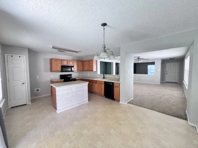 Open-concept kitchen featuring wood cabinetry, black appliances, a central island with a stone-look countertop, and tile-look flooring