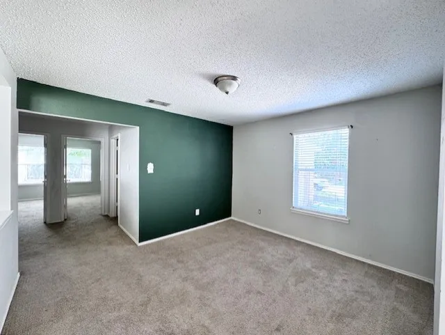Interior room featuring textured carpet flooring, a single window with blinds, and a textured ceiling