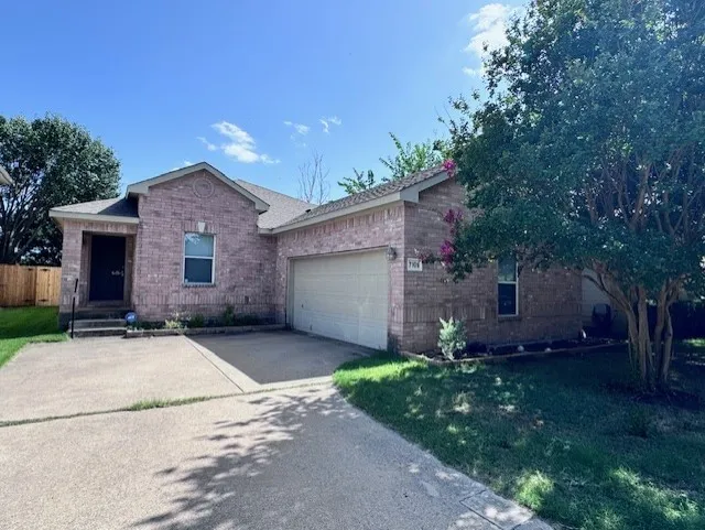 Brick exterior with an attached garage, concrete driveway, and established front yard landscaping