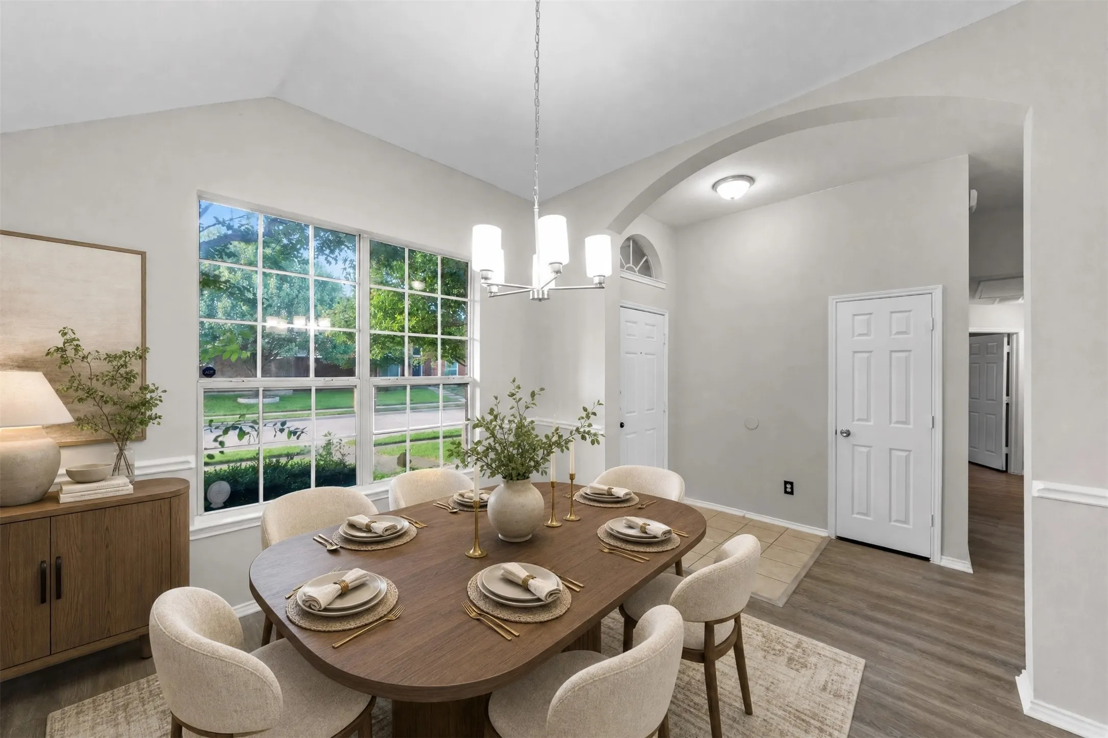 The spacious formal dining room offers vaulted ceilings, abundant natural light, fresh paint, new wood-look plank flooring, and an updated chandelier. A large picture window overlooks the mature trees in the front yard, creating an elegant setting for both everyday dining and special occasions. Virtual staged