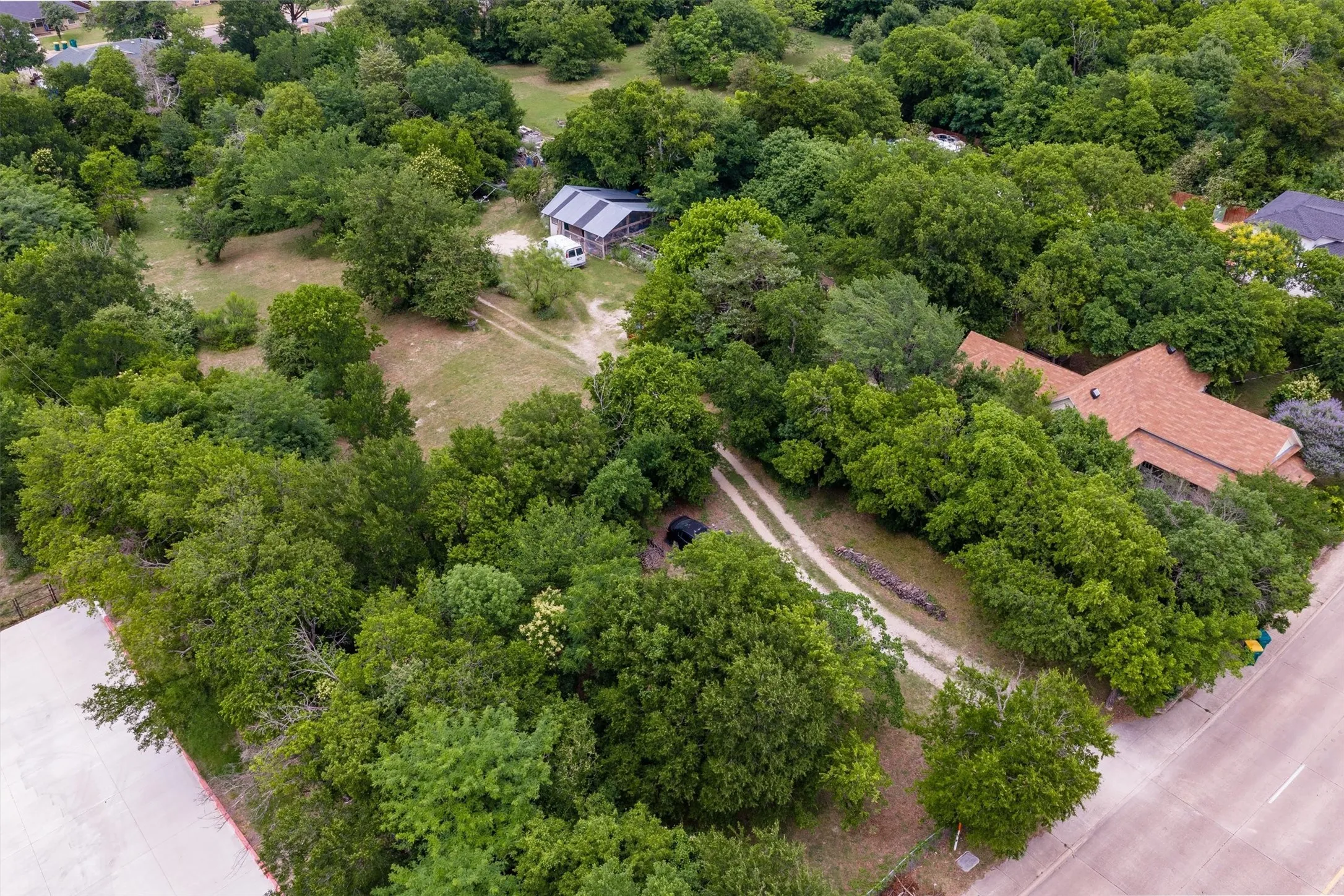 Expansive wooded property featuring a primary residence with a brown shingle roof, a secondary structure, and multiple dirt paths