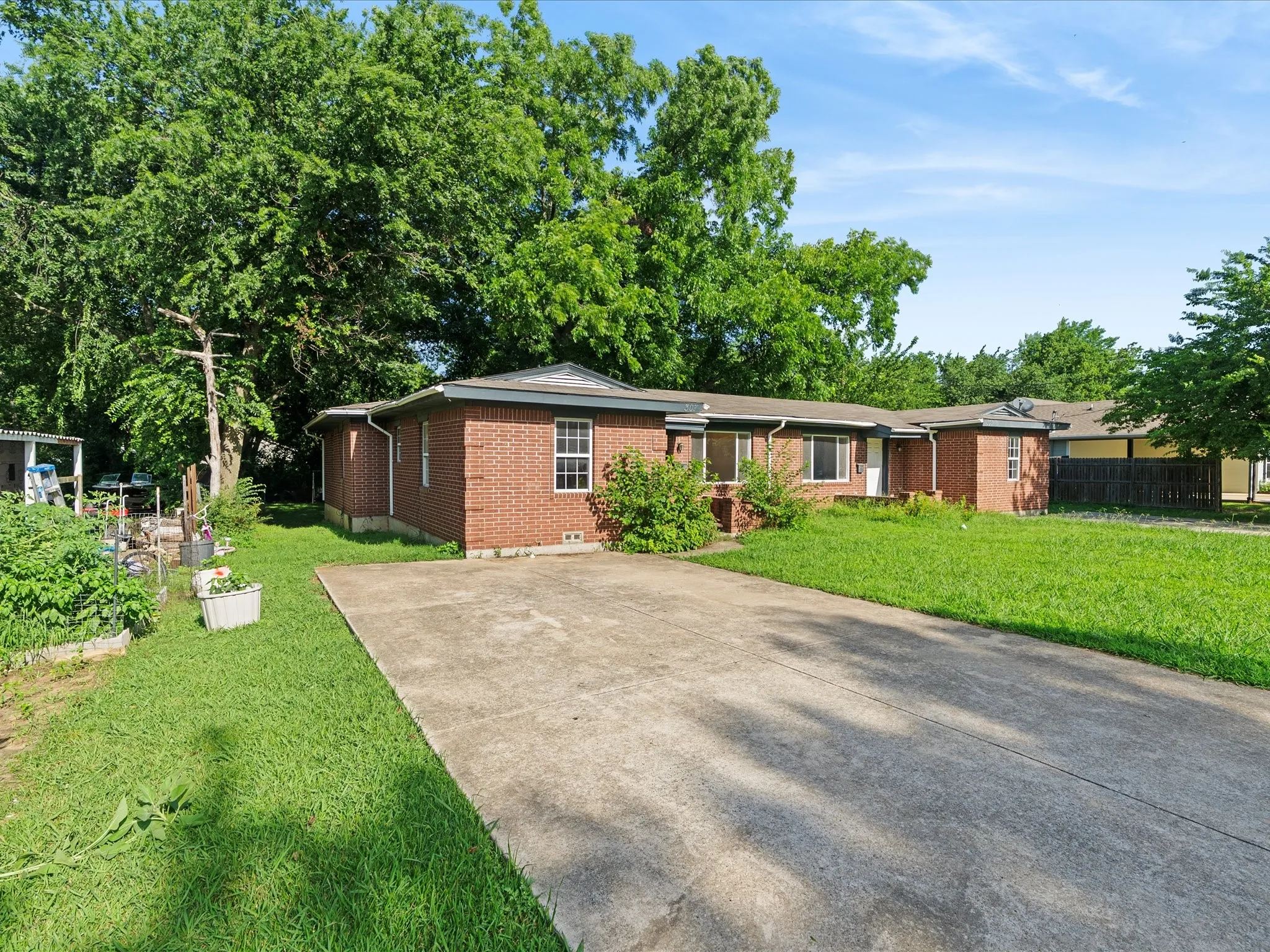 Brick exterior residence featuring an expansive front lawn, mature perimeter trees, a concrete driveway, and multiple windows