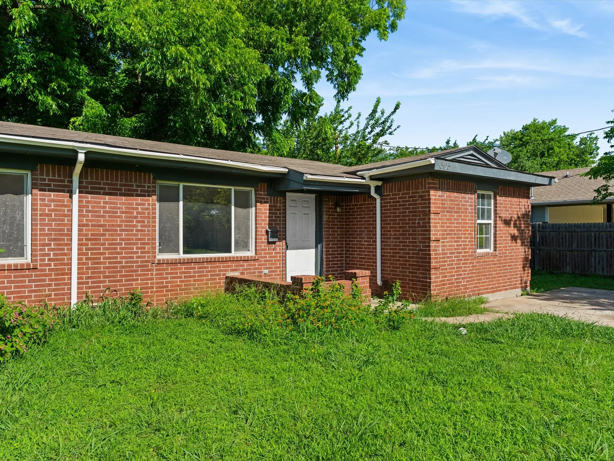 Brick exterior featuring multiple window openings, white window frames, a white entry door, and a partially paved driveway