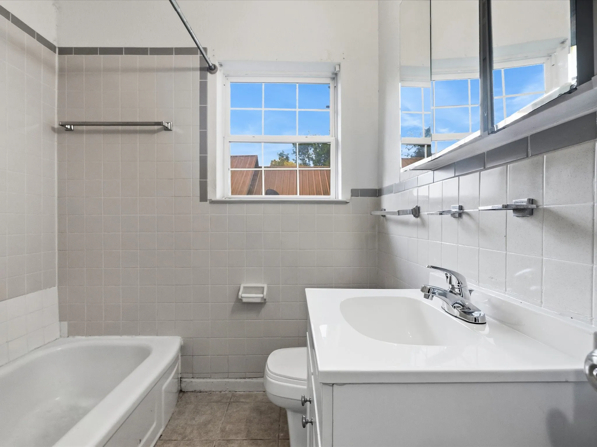 Bathroom featuring white subway tile walls with a contrasting gray border, a white vanity with an integrated sink, a chrome faucet, a window with grid panes, and a white bathtub
