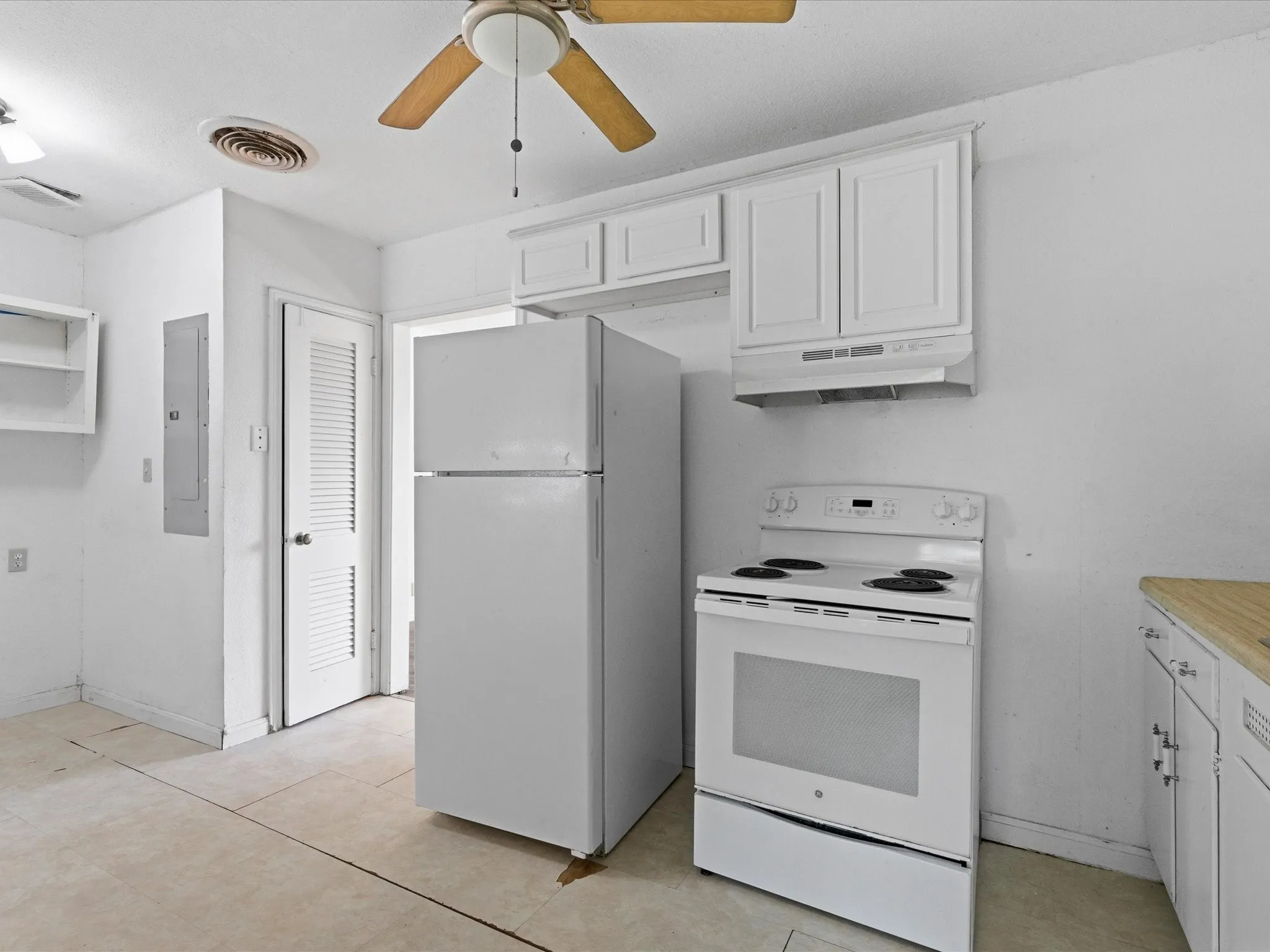 Kitchen featuring white appliances, a ceiling fan, upper cabinetry, and a louvered door