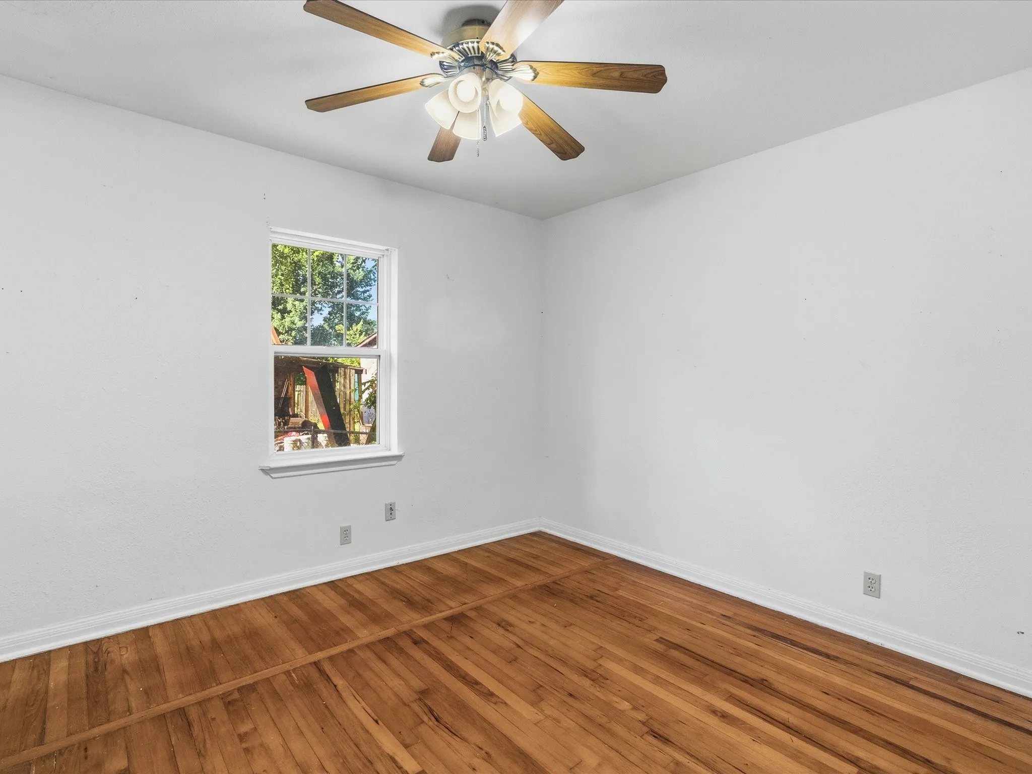 Room featuring wood-finish flooring, a ceiling fan with light fixture, and a window with white trim