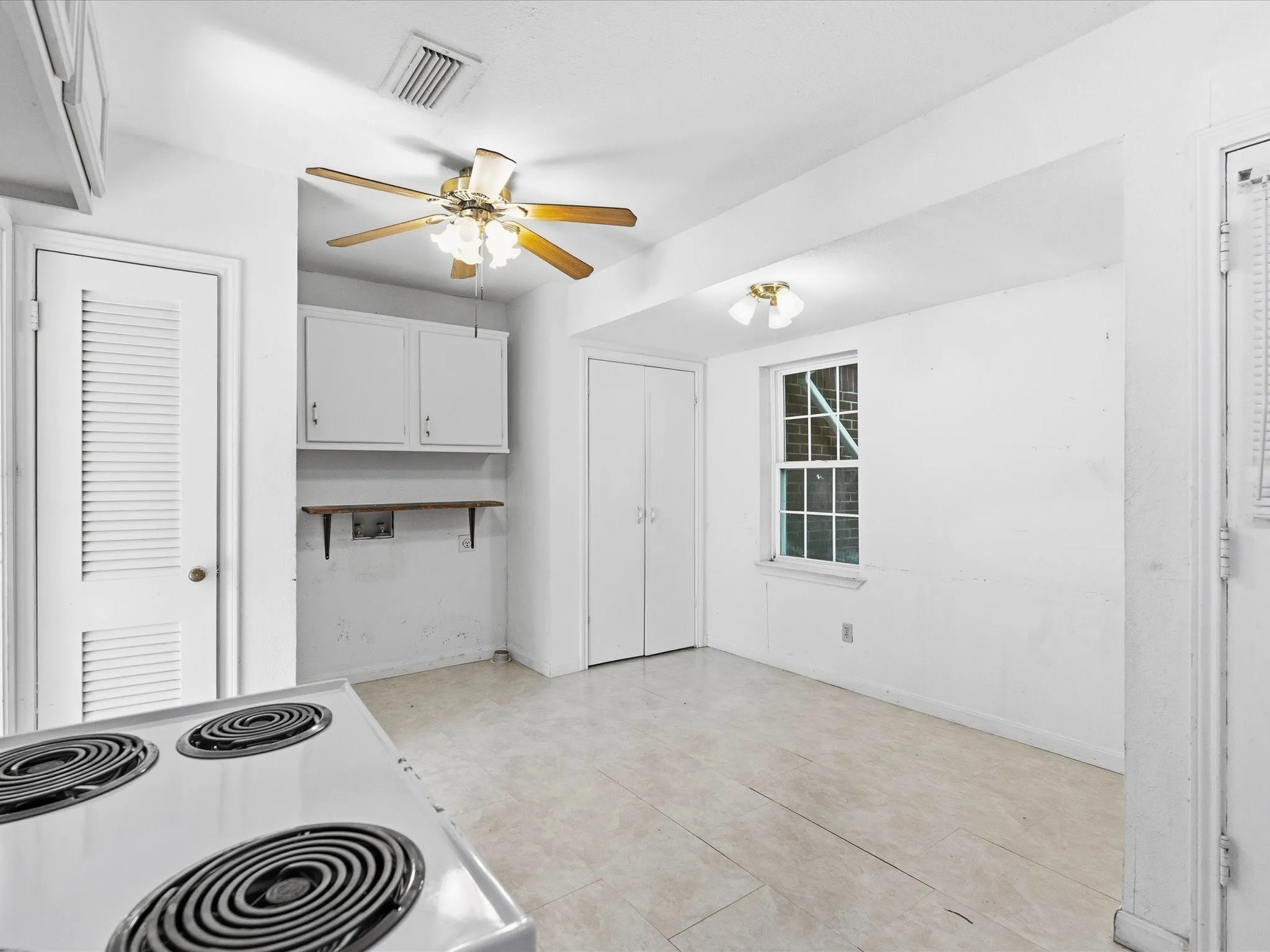 Kitchen area featuring white cabinetry, a built-in oven, tile flooring, a window with grid detailing, and a ceiling fan with light fixture