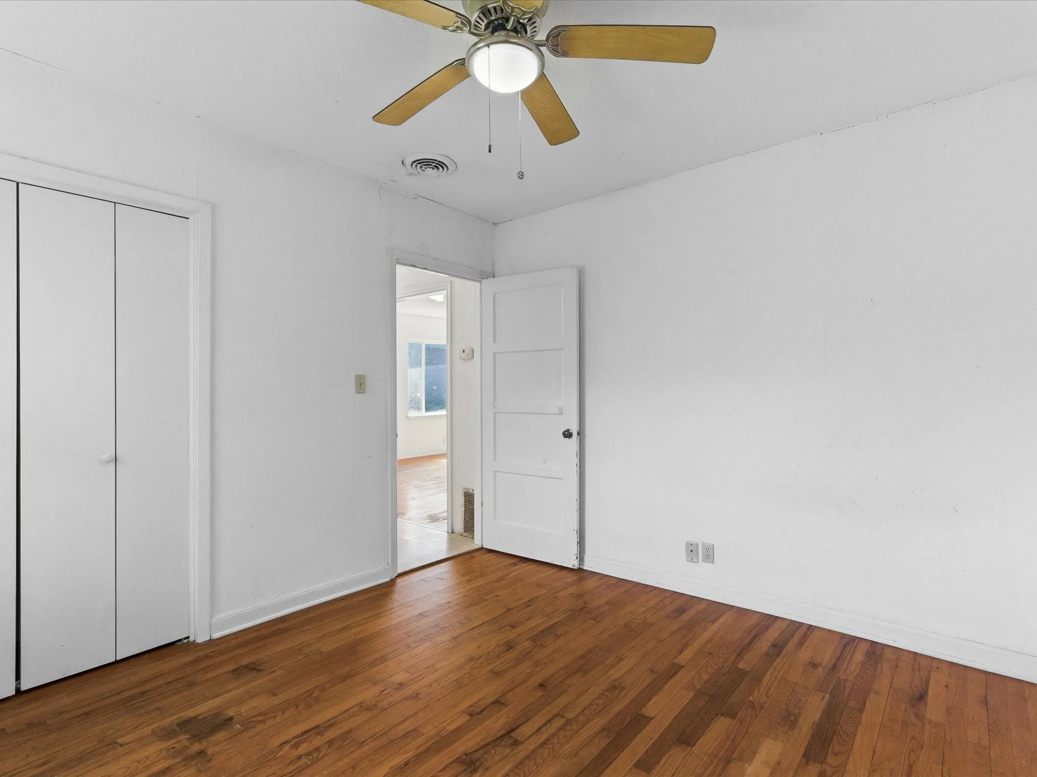Room featuring wood-finish flooring, white painted walls, a ceiling fan with light fixture, and a white paneled door