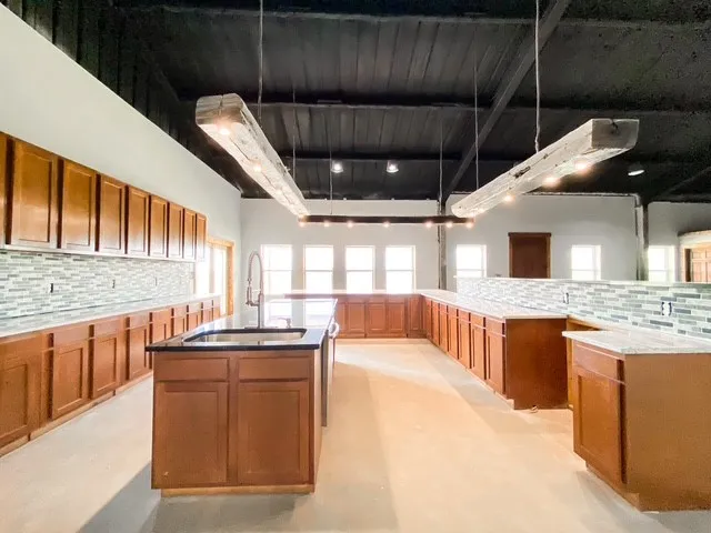 Stainless steel farmhouse sink in the island, granite counter tops, granite island and tile backsplash. Oak beams with LED lighting.