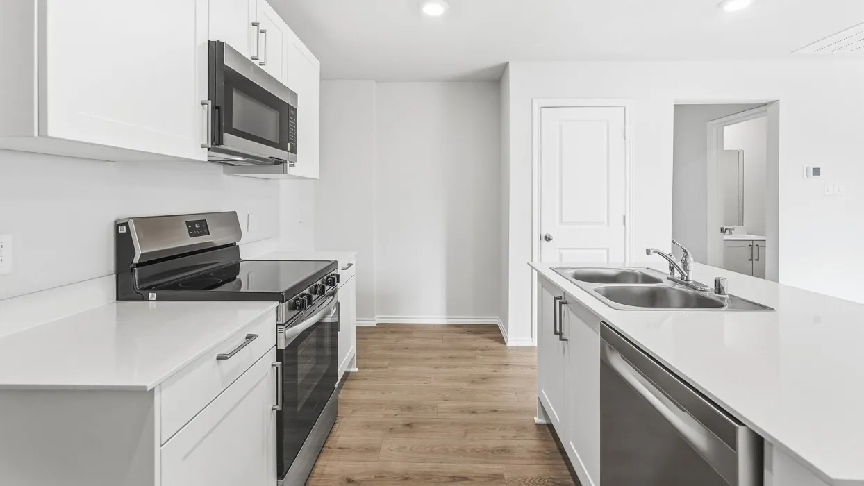 Kitchen featuring white cabinetry, stainless steel appliances, light-toned countertops, a double basin sink, and wood-finish flooring