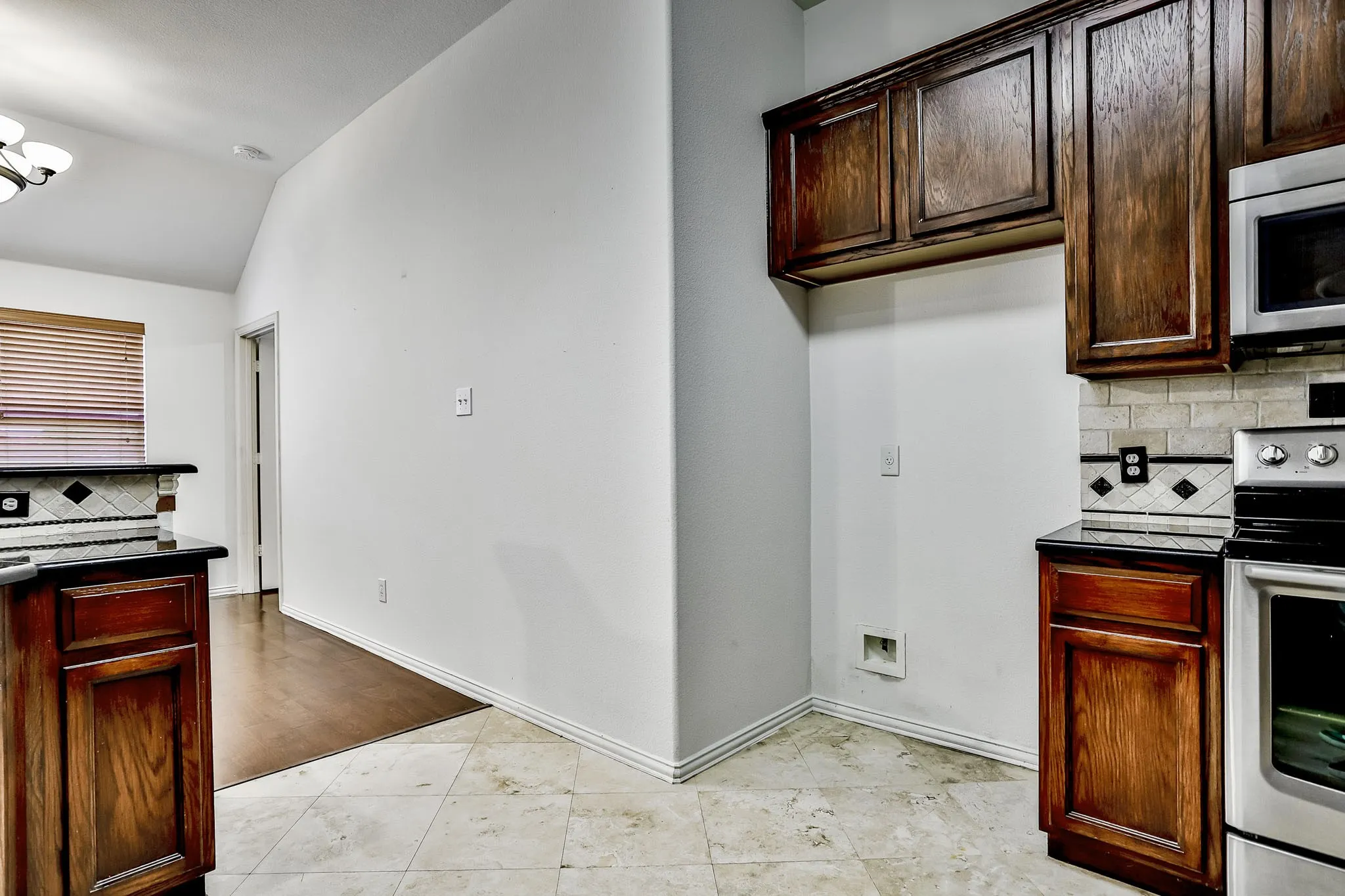 Kitchen featuring dark wood cabinetry, stainless steel oven with microwave, tile flooring, and a decorative tile backsplash