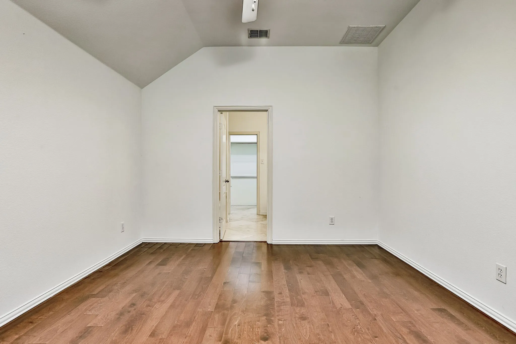 Room featuring wood-finish flooring, white baseboards, textured white walls, and a vaulted ceiling with a white ceiling fan