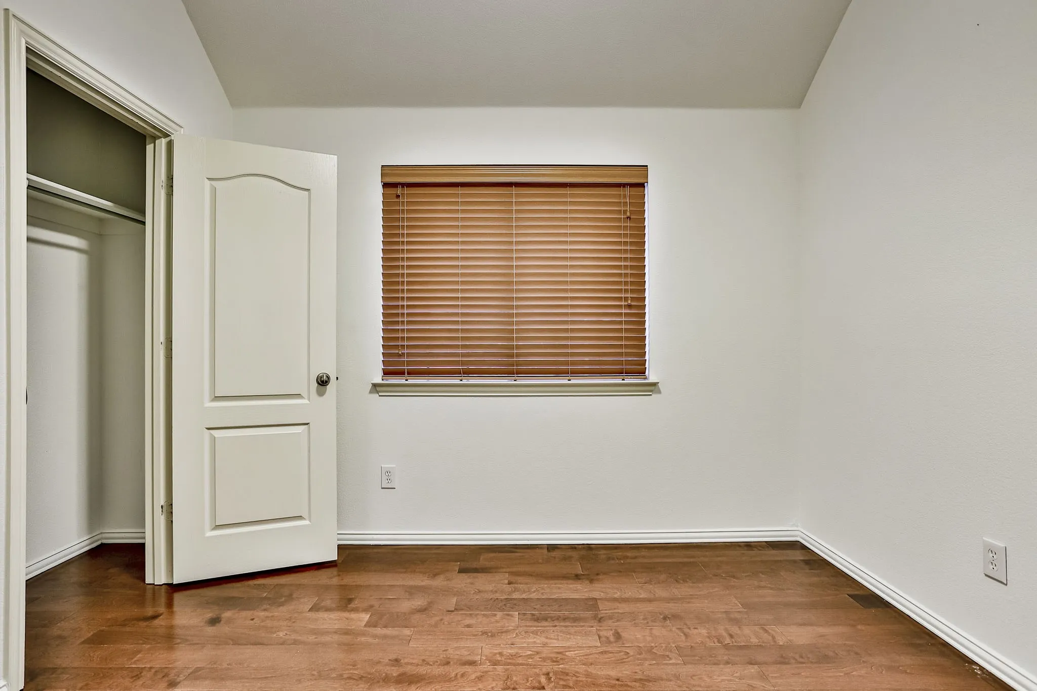 Room featuring wood-finish flooring, white walls, and a window with wood-tone blinds