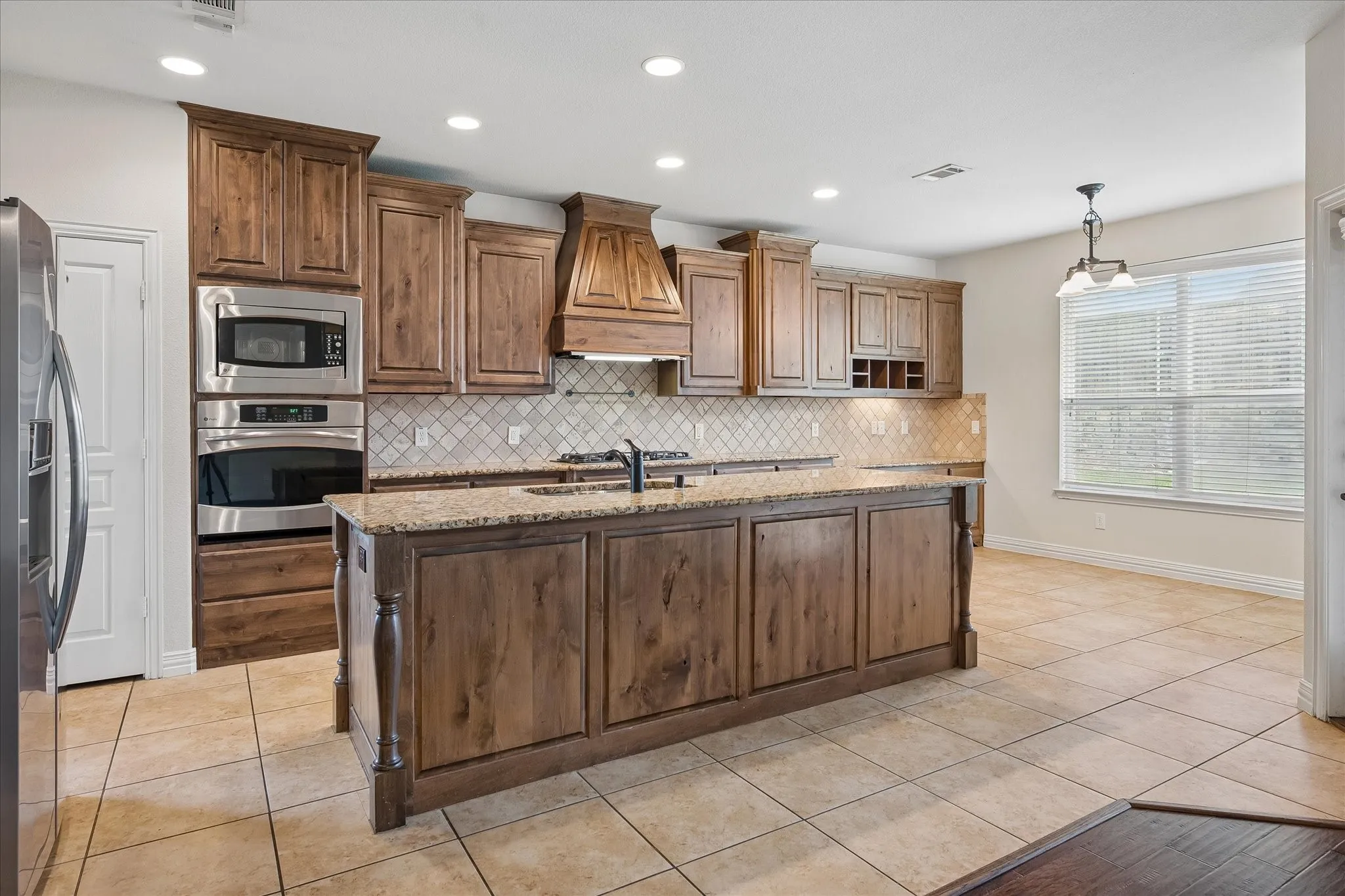 Kitchen featuring wood cabinetry, stainless steel appliances, a center island with a built-in sink, tiled backsplash, and recessed lighting
