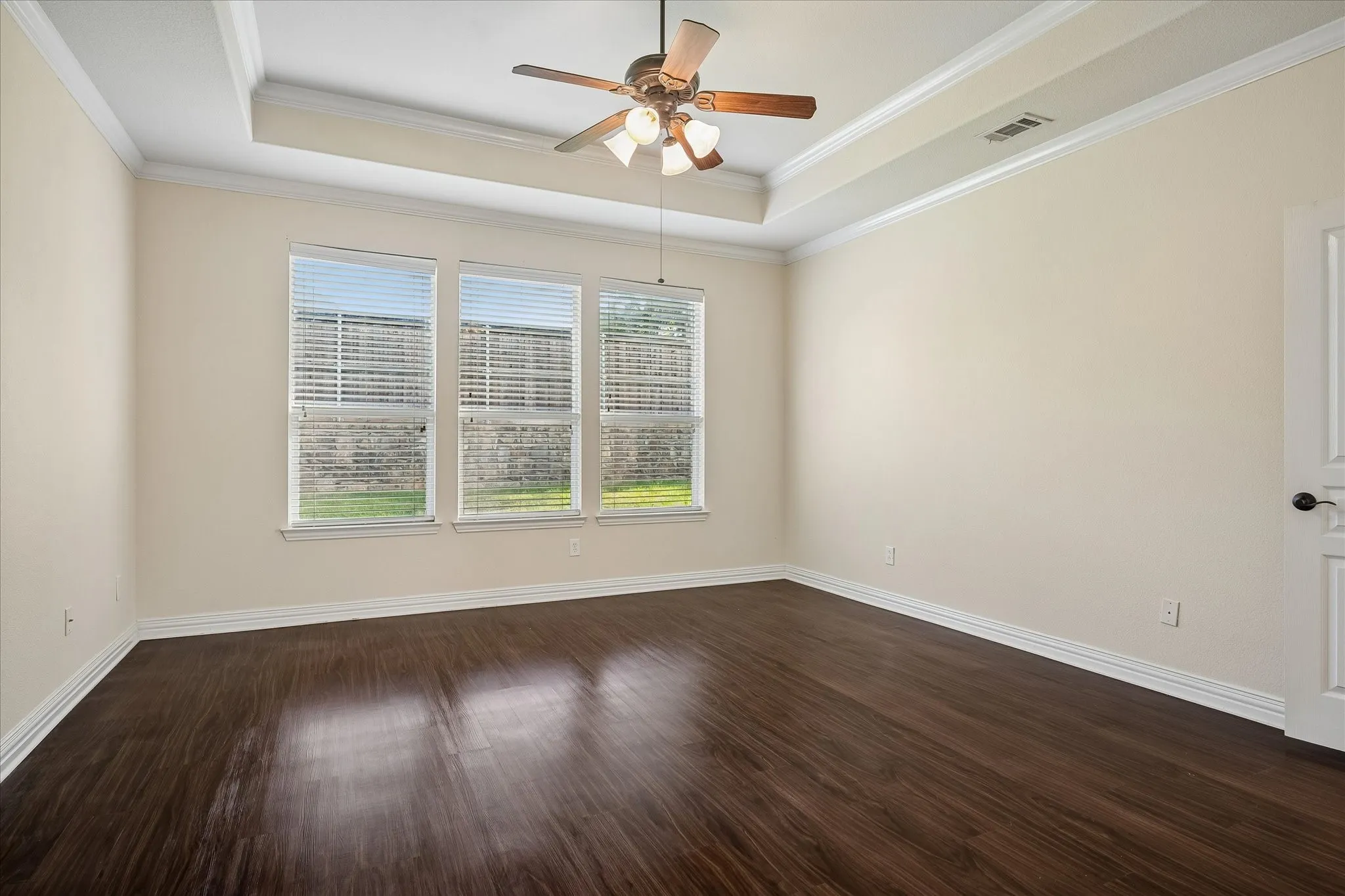 Tray ceiling with crown molding, ceiling fan with light fixture, wood-finish flooring, and multiple windows