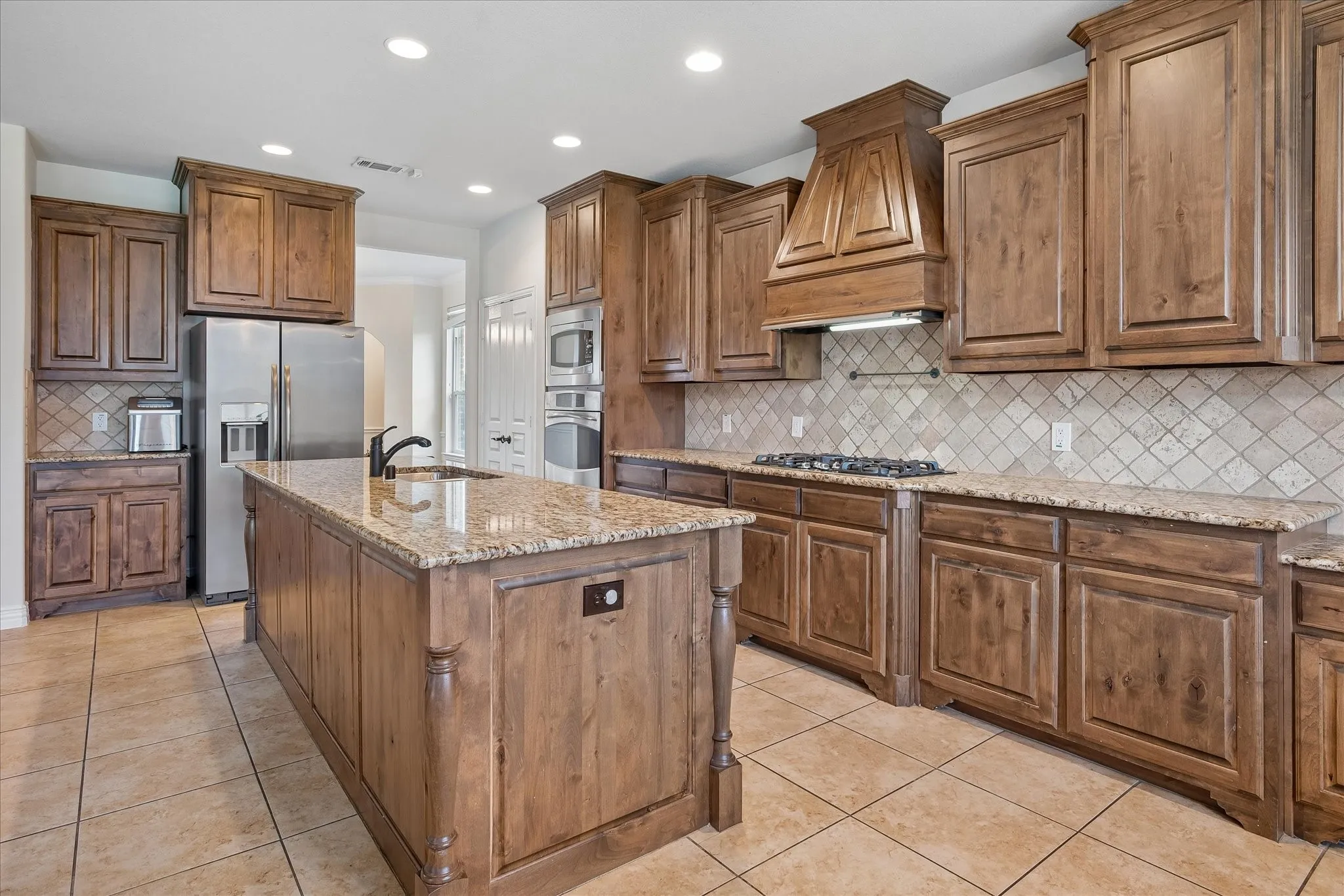 Kitchen featuring an island with a sink, stainless steel appliances, extensive cabinetry, granite countertops, and a tiled backsplash