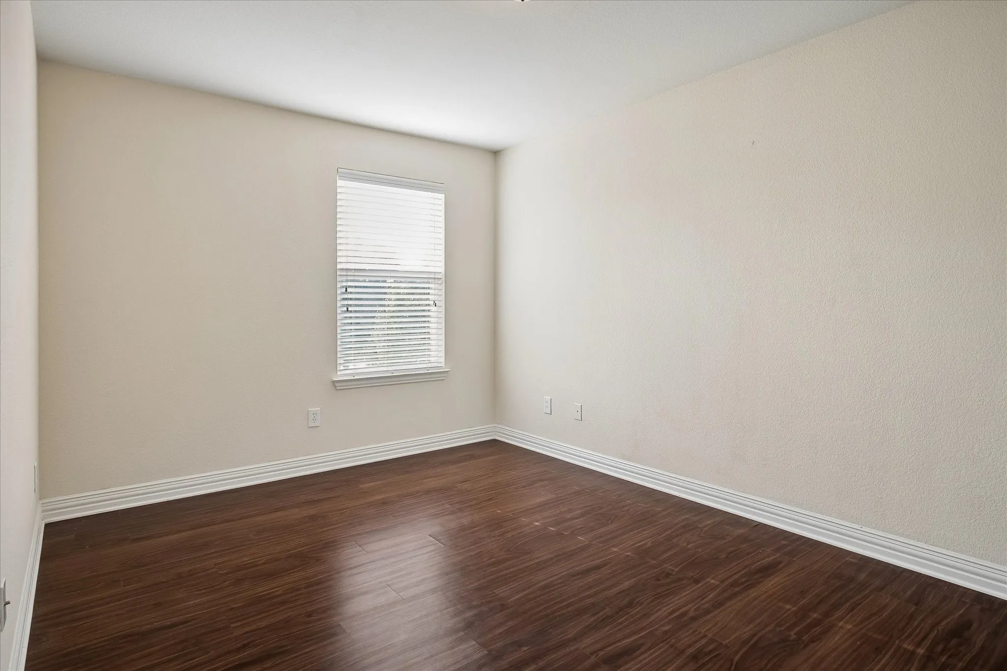 Wood-finish flooring with white trim and a single window with blinds