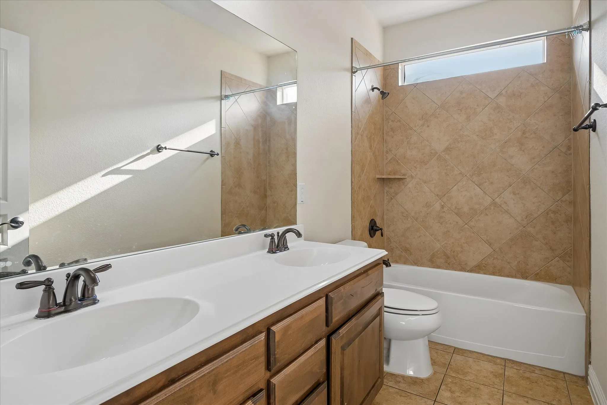 Dual basin vanity with bronze-finish fixtures, a large integrated mirror, and a wood-finish cabinet
