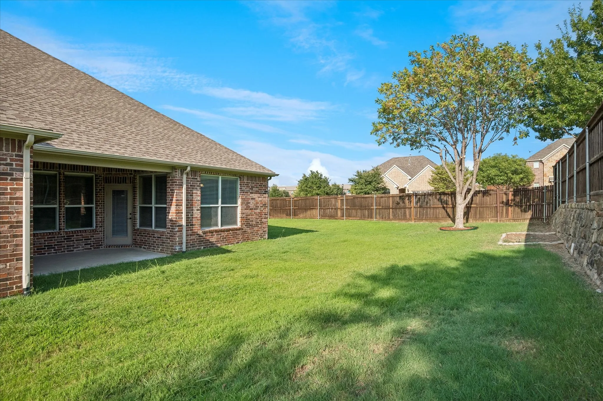 Expansive backyard featuring a manicured lawn, established tree, and wood privacy fencing