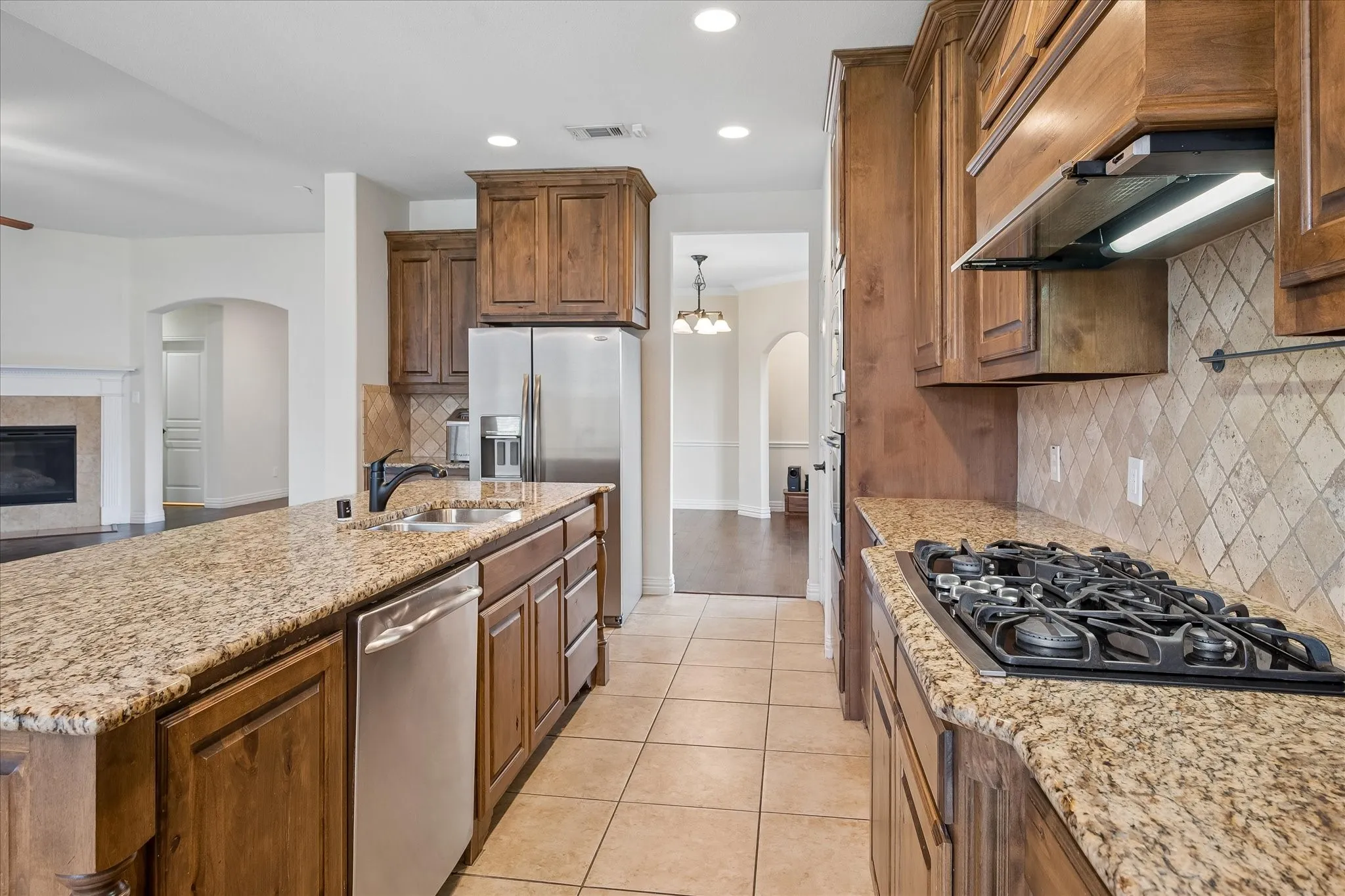 Kitchen featuring a gas cooktop, double basin sink, stainless steel appliances, granite countertops, and wood cabinetry